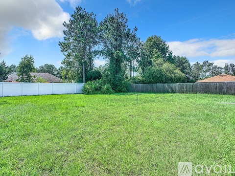 A grassy field with trees and a fence in the background.