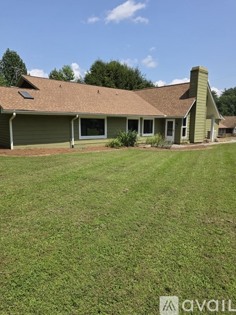 A house with a green roof and a chimney is surrounded by a grassy lawn.