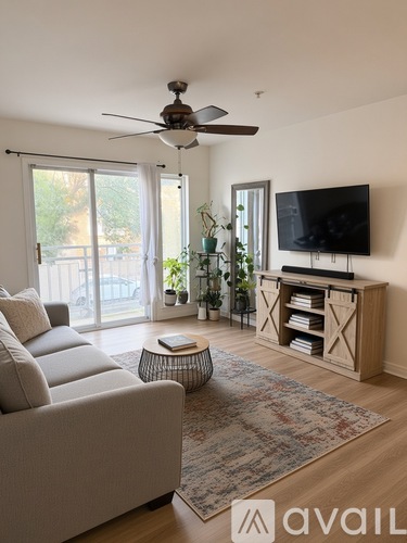 A living room with a grey sofa, a round table, a television, and a ceiling fan.