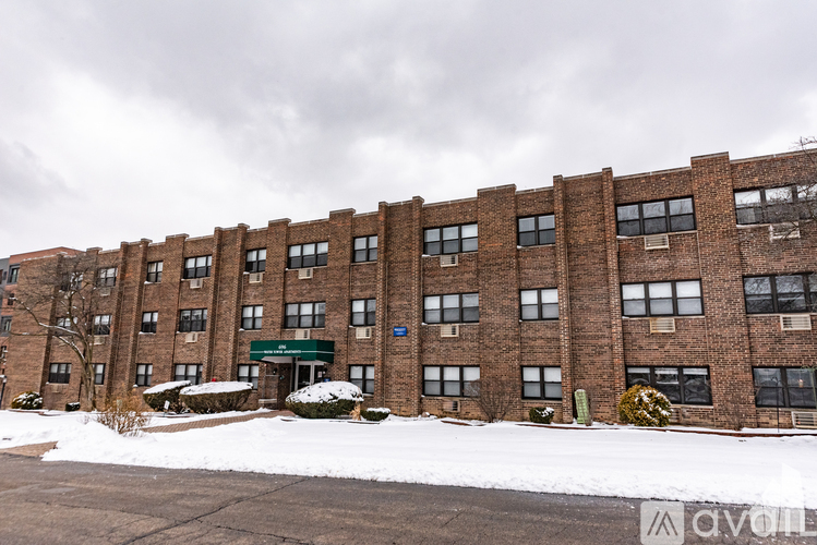 A large brick building with a green awning and a parking lot in front.