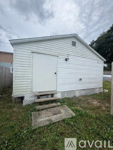 A small white shed with a door and a window is situated in a grassy area.