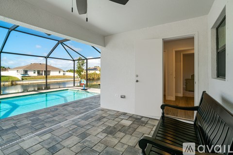 A black bench is in a room with a pool outside.