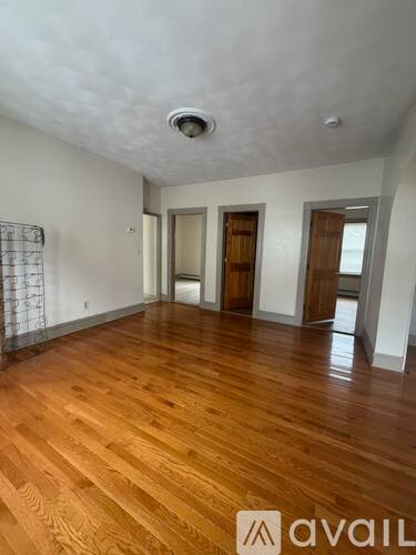A room with wooden flooring and white walls, with a window on the right wall.