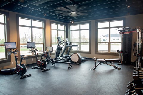 A gym with a row of stationary bikes and a fan.