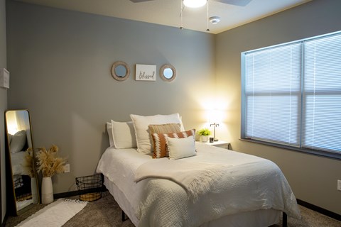 A bedroom with a bed, pillows, a mirror, and a window.
