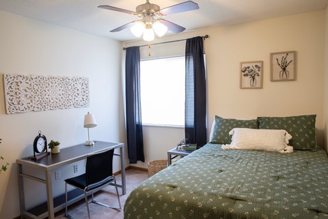 A bedroom with a bed, desk, chair, and window.