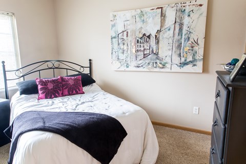 A bedroom with a bed, a dresser, and a painting on the wall.