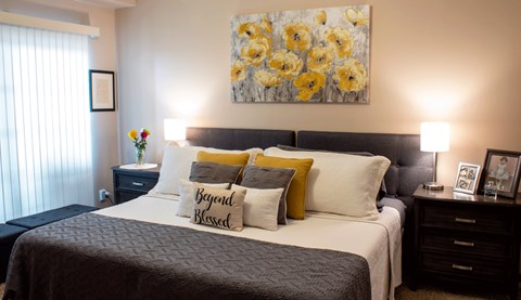 A bedroom with a bed, nightstands, and a painting of yellow flowers.