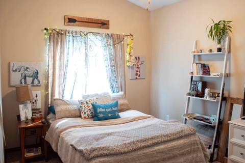 A bedroom with a bed, a bookshelf, and a window with curtains.
