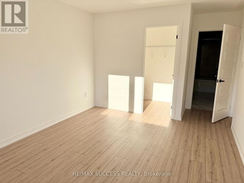 A room with wooden flooring and white walls, with a door open to a dark space.