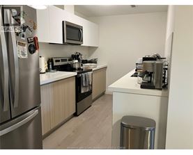 A kitchen with a refrigerator, microwave, oven, and a trash can.