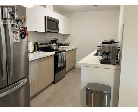 A kitchen with a refrigerator, microwave, oven, and a trash can.