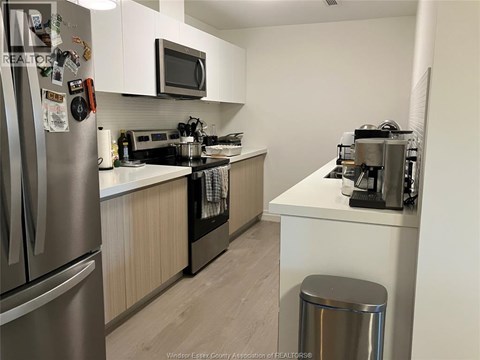 A kitchen with a refrigerator, microwave, oven, and a trash can.