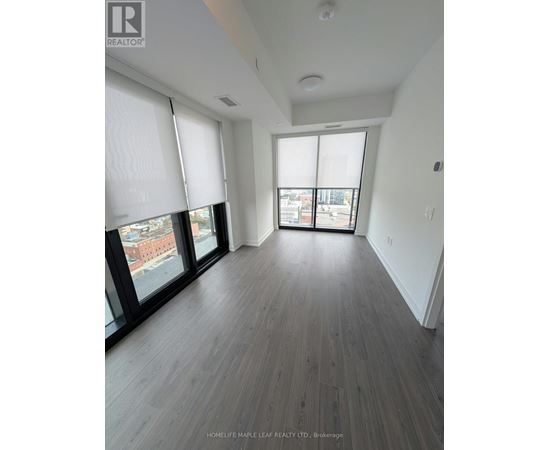 A spacious room with wooden flooring and large windows.