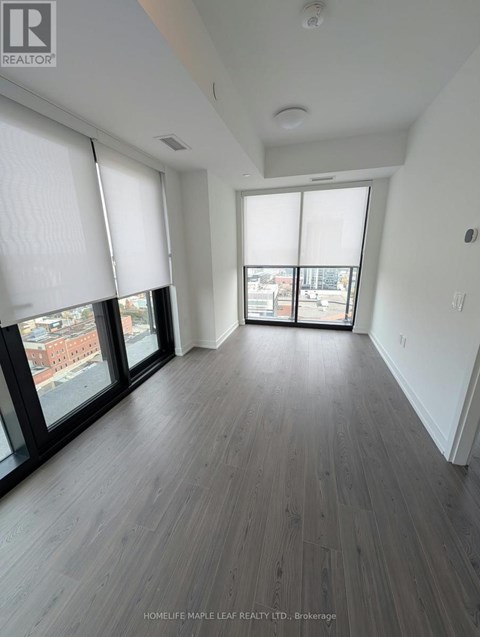 A spacious room with wooden flooring and large windows.