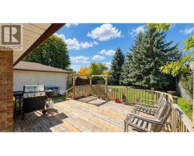A wooden deck with chairs and a grill is surrounded by a fence and trees.