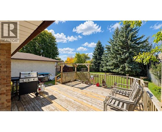A wooden deck with chairs and a grill is surrounded by a fence and trees.