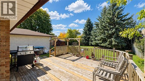 A wooden deck with chairs and a grill is surrounded by a fence and trees.