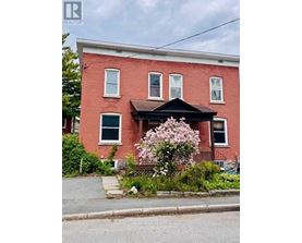 A red brick house with a black front porch and a flowering bush in front.