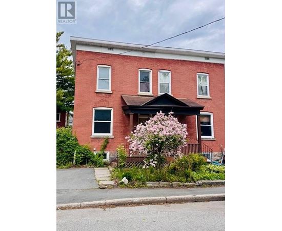 A red brick house with a black front porch and a flowering bush in front.