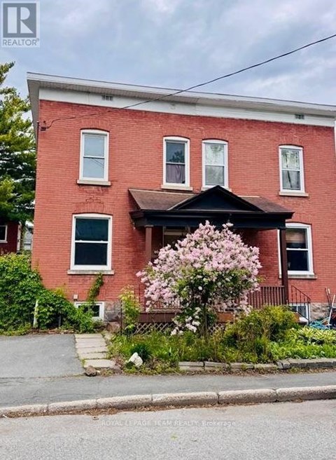 A red brick house with a black front porch and a flowering bush in front.