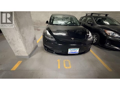 A black Tesla car is parked in a parking spot with the number 10 on the ground.