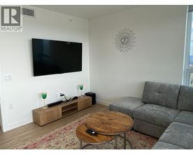 A living room with a grey couch, a wooden coffee table, and a flat screen TV mounted on the wall.