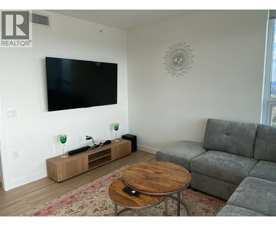 A living room with a grey couch, a wooden coffee table, and a flat screen TV mounted on the wall.