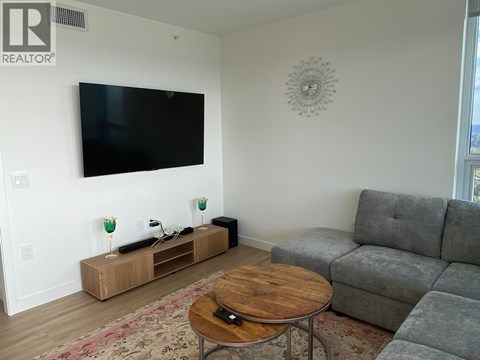 A living room with a grey couch, a wooden coffee table, and a flat screen TV mounted on the wall.
