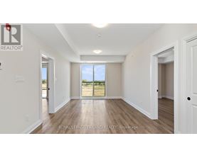 A spacious room with white walls and wooden flooring, with a large window and a door visible.