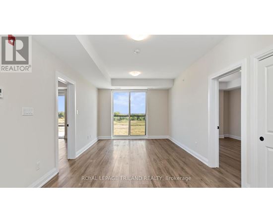 A spacious room with white walls and wooden flooring, with a large window and a door visible.