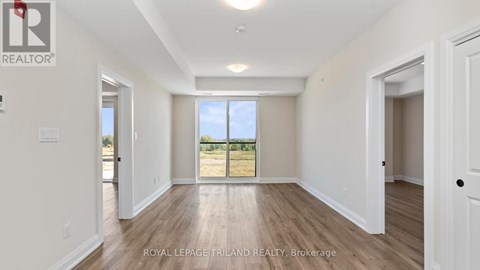 A spacious room with white walls and wooden flooring, with a large window and a door visible.