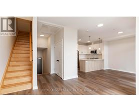 A room with a staircase and a kitchen area is on the market with Royal LePage Triland Realty.