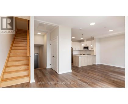 A room with a staircase and a kitchen area is on the market with Royal LePage Triland Realty.