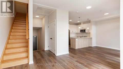A room with a staircase and a kitchen area is on the market with Royal LePage Triland Realty.