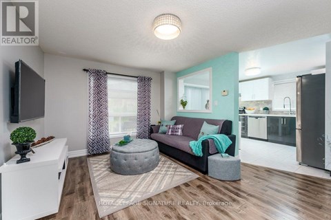 A living room with a grey ottoman and a grey couch with a green throw on it.