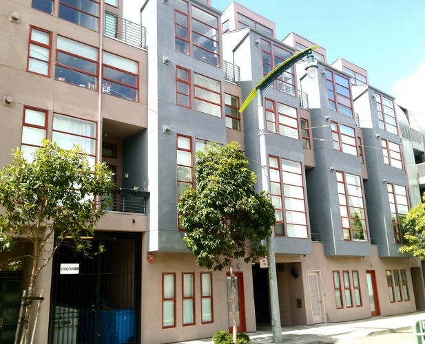 A modern apartment building with balconies and trees in front.