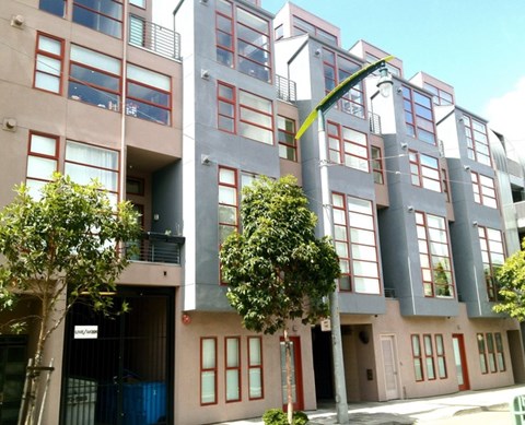 A modern apartment building with balconies and trees in front.