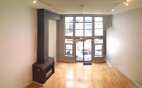 A wood stove is in a corner of a room with a large window.