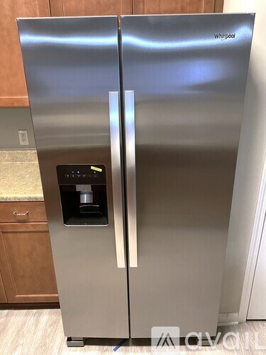 A Whirlpool stainless steel refrigerator with a water and ice dispenser in the middle of the door.