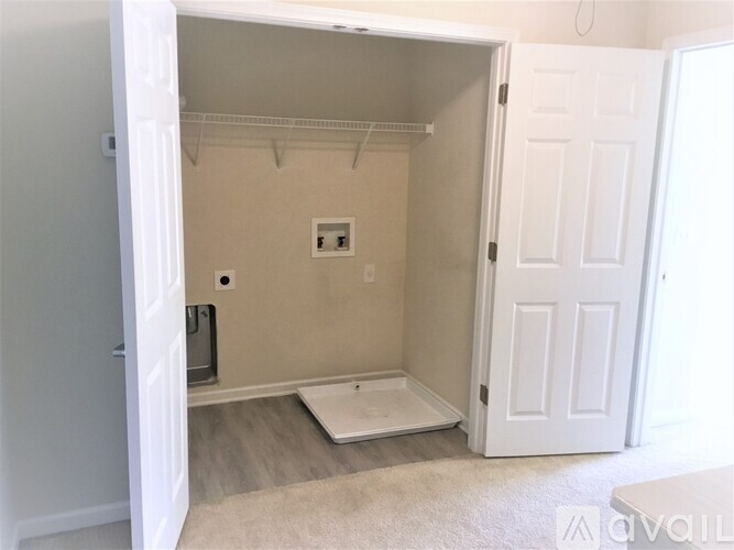 A white door is open to a small bedroom with a bed and a small table.