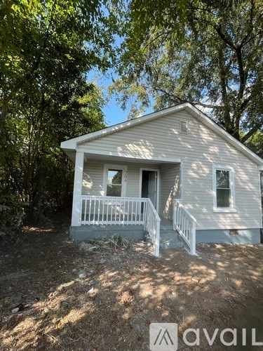 A small house with a porch is surrounded by trees.
