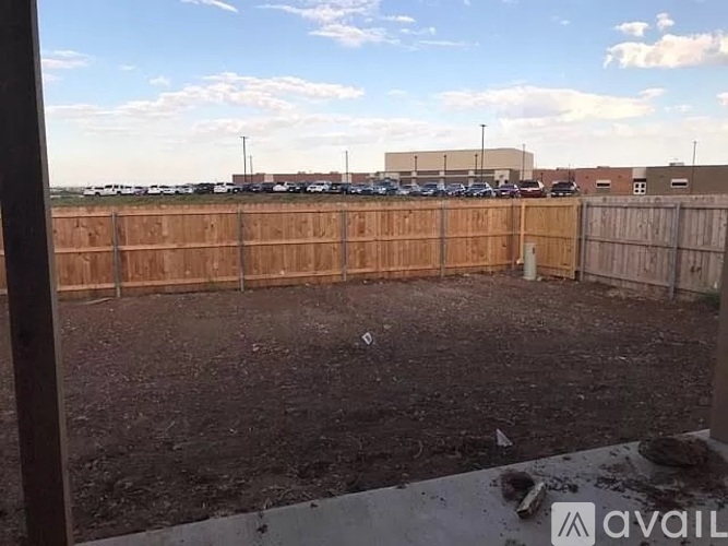 A parking lot with a wooden fence in the foreground and a building in the background.