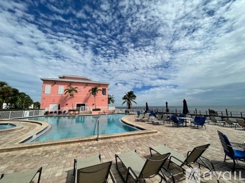 A pool area with chairs and a pink building.