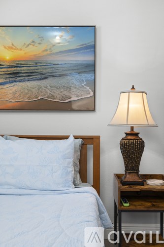 A bedroom with a bed, a nightstand with a lamp and a painting on the wall.