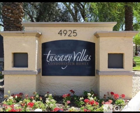 A sign for Tuscany Villas Condominium Homes is surrounded by flowers.