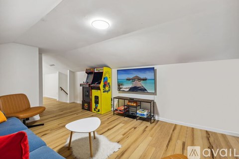A living room with a yellow arcade machine and a painting of a mountain scene on the wall.
