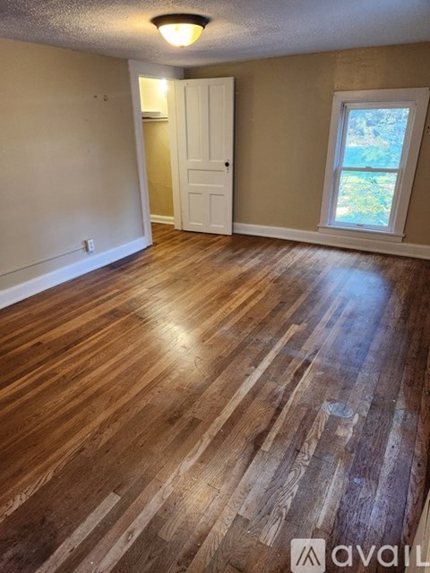 A room with wooden flooring and a window showing a view of trees outside.