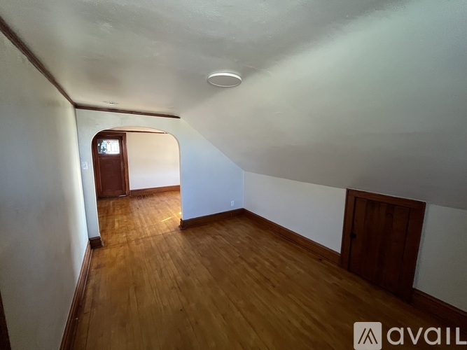 A room with wooden floors and white walls, with a door on the right and a window on the left.