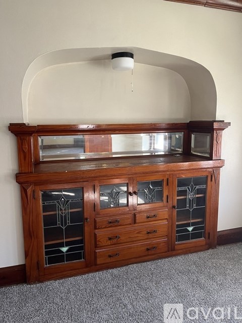 A wooden cabinet with glass doors and drawers is in the corner of a room.